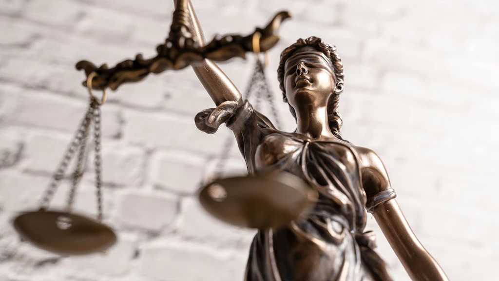 Auf dem Bild ist eine Justitia-Figur vor einer weißen Steinmauer zu sehen