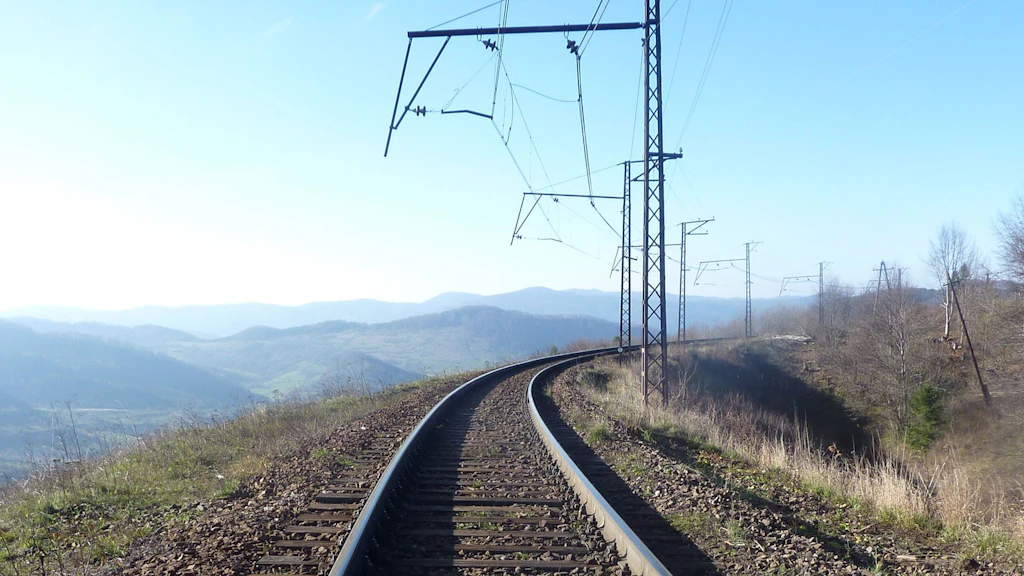 Binario ferroviario con linea aerea che curva attraverso un paesaggio collinare
